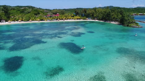 Luftbild-In-Zeitlupe-Von-Menschen,-Die-In-Der-Nähe-Des-Strandes-Eines-Resorts-Am-Honduranischen-Karibischen-Meer-Paddeln
