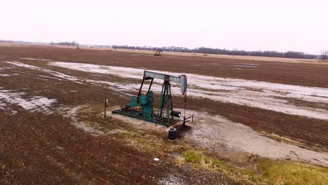 A-steady-overhead-shot-from-a-drone-of-a-pump-jack-collecting-oil-from-an-oilfield-in-a-field-during-the-winter