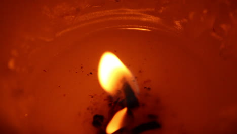 Very-close-view-of-an-orange,-red-candle-with-melted-wax-insde-the-crate,-blurring-until-becomes-an-abstract-moving-bulb-of-light