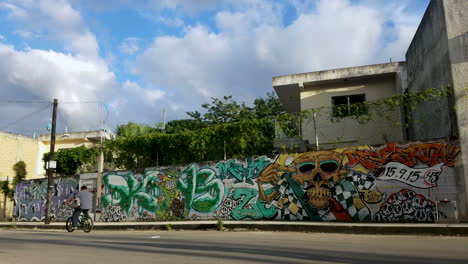 Graffiti-wall-in-downtown-Playa-Del-Carmen,-People-are-riding-bikes-on-the-street