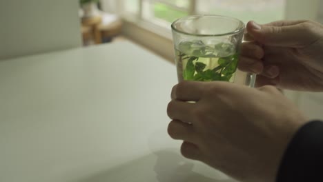Hands-holding-herbal-tea-on-table-in-apartment---then-man-drinks-and-puts-back-glass