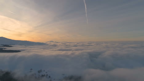 Antenne,-Drohnenaufnahme,-über-Wolken,-Vor-Schneebedecktem-Wald,-Berggipfeln-Und-Sonnenuntergangsfarben