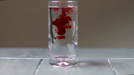Dropping-drops-of-red-food-dye-into-a-single-glass