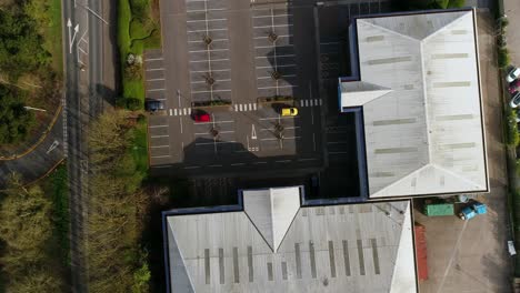 Top-down-aerial-of-an-almost-empty-Car-Park-in-a-small-retail-park,-with-three-cars-all-different-colours