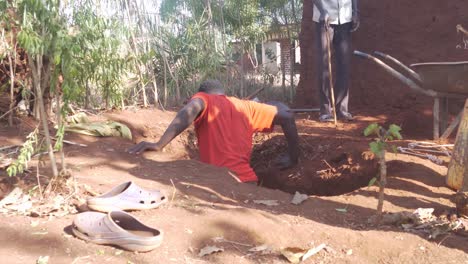 African-man-in-a-rural-village-crawling-down-into-a-hole-which-is-being-dug-out-into-a-pit-latrine