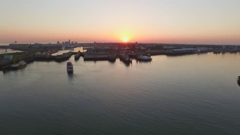 Aerial:-The-smaller-port-of-Vlissingen,-with-cargo-ships-passing-by,-during-sunset