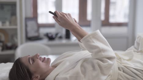 Woman-smiling-and-texting-on-her-phone-while-laying-on-the-table-at-a-spa