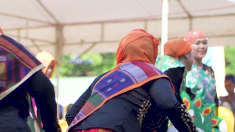 Women-wearing-matching-orange-scarves-on-their-heads-perform-a-traditional-dance-in-front-of-an-audience-during-a-celebration-event