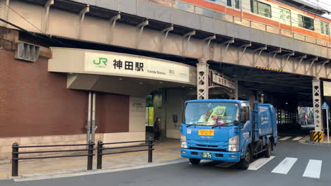 A-garbage-truck-passes-in-front-of-the-West-gate-of-Kanda-Station-during-a-train-passes-overhead