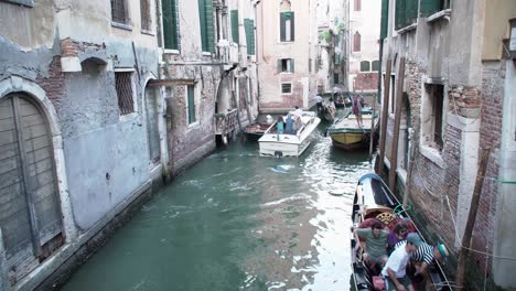 Gondolas---boats-carrying-tourists-pass-through-a-busy-Venetian-canal-in-Venice,-Italy