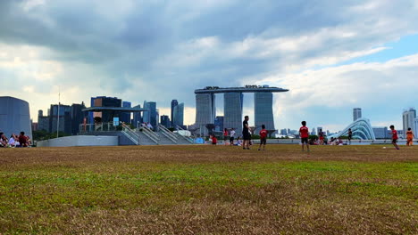 Time-lapse-shot-of-children-playing-soccer-in-an-open-field-with-a-Coach-and-Marina-Bay-Sand-landmark-in-the-background