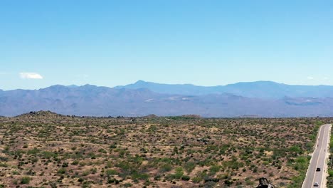Aerial-pan-right-from-open-desert-to-a-lonely-desert-highway-where-bicyclists-share-the-road-with-cars,-Scottsdale,-Arizona