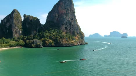 Low-aerial-shot-of-long-tail-boat-and-large-limestone-karsts-in-Railay-Beach,-Ao-Nang,-Krabi,-Thailand