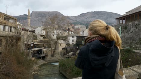 Back-View-clip-of-blonde-woman-looking-at-the-sights-of-Old-Town-in-Mostar-while-standing-on-a-bridge-circa-November-2018
