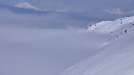 Time-lapse-in-the-French-Alps-in-winter,-showing-inverted-low-cloud-rolling-up-the-side-of-a-mountain-with-a-distant-ski-lift