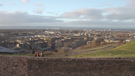 Panning-shot-from-Calton-hill-with-people-walking-in-the-foreground-with-nice-sunset-light-and-clouds-overlooking-the-city-of-Edinburgh,-Scotland-and-Atlantic-Ocean-in-the-background