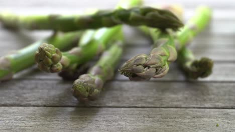 Footage-of-a-bunch-of-fresh,-green-asparagus-falling-on-to-a-wood-table