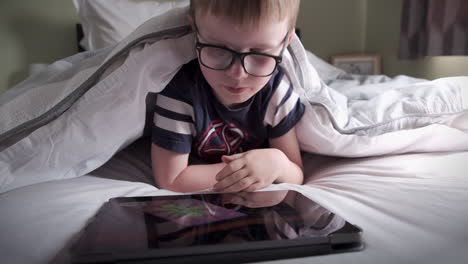 A-six-years-old-boy-reading-a-computer-tablet-while-lying-in-his-bed
