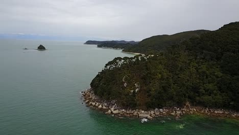 Aerial-view-flying-over-golden-sand-beach-and-beautiful-green-mountains-in-Abel-Tasman-National-Park,-Nelson,-New-Zealand