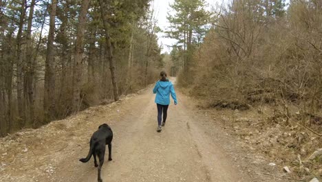 Girl-walking-on-mountain-trail-in-forest-with-black-dog