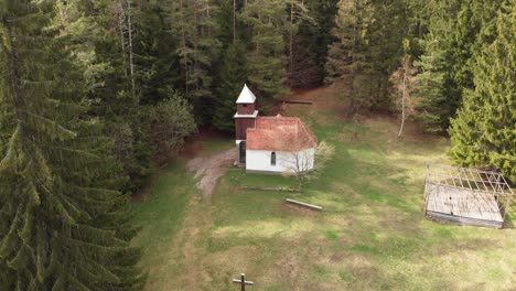 Aerial-pulling-back-shot-of-an-old-church-in-the-middle-of-a-pine-forest-in-the-Carpathian-Mountains,-Romania