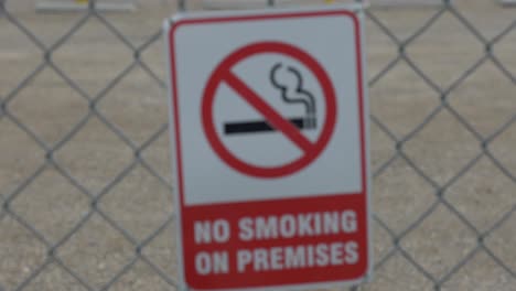 A-focus-pull-red-and-white-no-smoking-on-the-premises-sign-on-a-chain-linked-fence