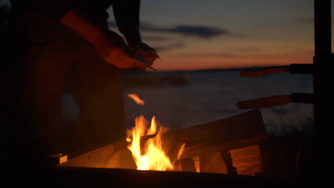 Man-lighting-camping-fire-by-the-sea-at-dusk