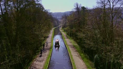 A-Narrow-Boat-heading-up-stream-after-Crossing-the-Pontcysyllte-Aqueduct,-designed-by-Thomas-Telford,-located-in-the-beautiful-Welsh-countryside,-famous-Llangollen-Canal-route,-as-cyclists-go-by