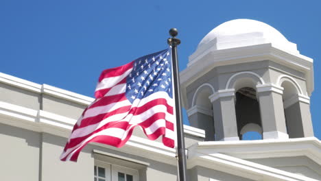 Una-Bandera-Estadounidense-Ondeando-En-El-Viento-Frente-A-Un-Edificio-Histórico-Blanco-En-El-Viejo-San-Juan,-Puerto-Rico