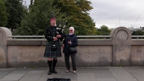 Old-lady-dancing-next-to-bagpiper-playing-in-Edinburgh-Scotland-for-tourists