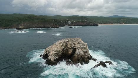 Aerial-drone-shot-of-a-big-rock-formation-and-the-coastline-of-Zipolite,-Oaxaca