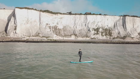 Junger-Mann-Stand-Up-Paddle-Boarding-Im-Meer-Mit-Weißen-Klippen-Von-Dover-Im-Hintergrund