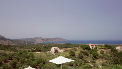 Aerial-Pedestal-of-Luxury-Greek-Villa-Patio---Loungers-revealing-Coastline-in-the-Distance-in-Crete,-Greece