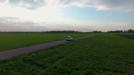 Aerial-Drone-Shot-of-a-White-Car-Driving-on-a-Narrow-Country-side-Road-in-The-Evening-in-South-Sweden-Skåne