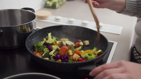 Woman-hands-cooking-vegetables-on-frying-pan-in-the-kitchen