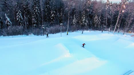 Seitliche-Luftaufnahme-Eines-Snowboarders,-Der-In-Einem-Funpark-Von-Einer-Piste-Springt