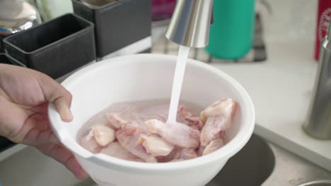 Man's-hand-turns-on-faucet-to-run-water-over-raw-chicken