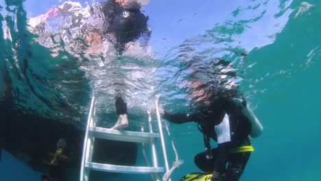 A-underwater-view-of-scuba-divers-entering-a-boat-using-a-ladder