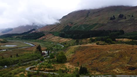 Cinematic-drone-shot-of-scottish-highland-village-with-river-and-misty-mountains-in-background