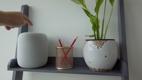 Static-Shot-of-Man-Double-Tapping-an-Apple-HomePod-on-top-of-Modern-Looking-Bookshelf-adjacent-to-a-Pencil-Holder---Plant