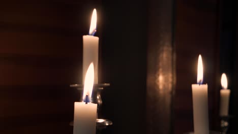 Mid-Handheld-Shot-of-a-Few-Candles-on-a-Silver-Candlestick-with-Wooden-Walls-and-a-Mirror-in-The-Background