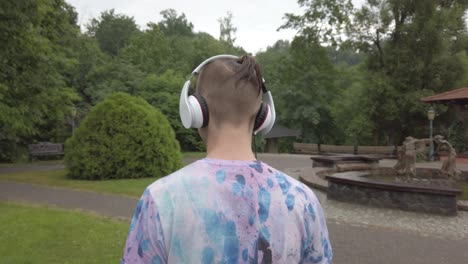Teenager-boy-listen-to-the-music-with-the-headphones-on-while-doing-a-walk,-the-camera-man-follows-from-the-back,-24-frames-per-second-at-4k
