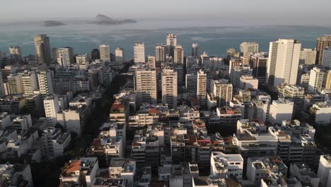 Luftaufnahmen,-Die-Das-Viertel-Ipanema-In-Rio-De-Janeiro-Mit-Hohen-Und-Niedrigen-Gebäuden-Zeigen,-Die-Bei-Sonnenaufgang-Inseln-Direkt-Vor-Der-Küste-Enthüllen