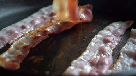 Man-Chef-cooking-for-breakfast:-turning-crispy-bacon,-rich-in-fat-and-colour,-sizzling-and-smoking-in-a-hot-pan