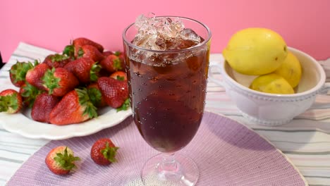 pouring-tall-glass-of-ice-tea-on-vibrant-pink-summer-background-with-strawberries-and-lemons