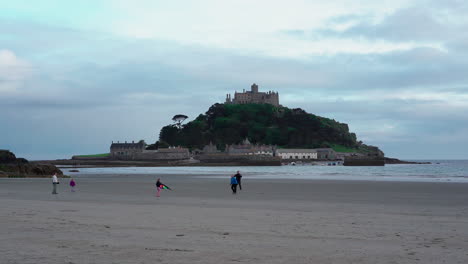 Children-playing-with-a-kite-on-the-beach-of-Marazion-in-Cornwall-with-the-english-medioeval-castle-and-church-of-St-Michael's-Mount-behind