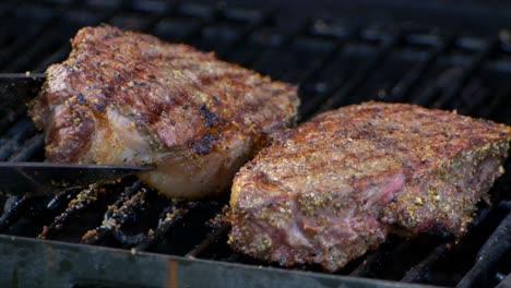Eine-Fleischzange-Hebt-Ein-Fast-Gekochtes-Saftiges-Rib-Eye-Steak-Auf-Einen-Grill-Und-Drückt-Darauf-Und-Ein-Weiteres-Steak