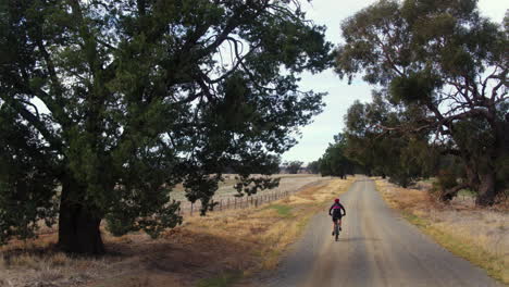Drohne-Nach-Weiblichem-Mountainbiken-Entlang-Der-Unbefestigten-Landstraße-Im-Ländlichen-Australien