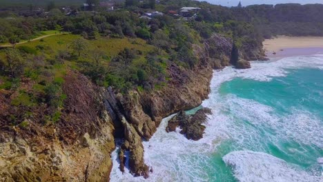 Tilting-aerial-view-of-wild-rocky-coastline-with-turquoise-blue-water-and-sea-foam