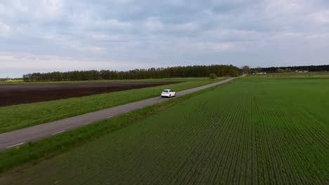 Aerial-Drone-Following-Shot-of-a-White-car-Driving-on-a-Narrow-Country-side-Road-in-South-Sweden-Skåne